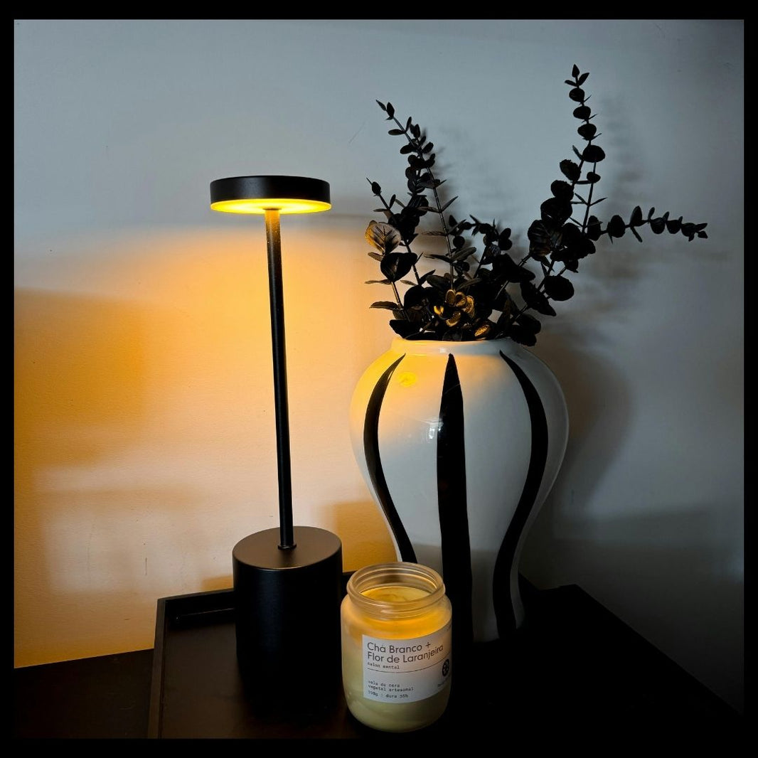 Black lamp, white vase with plants, and candle on a table against a blurred background